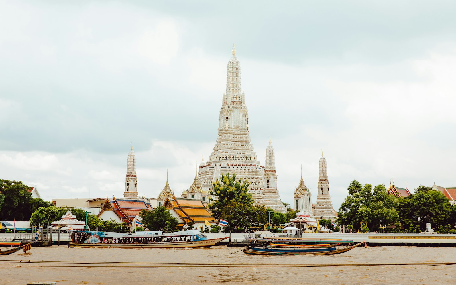 Wat Arun temple rising above the Chao Phraya river with boats passing in Bangkok