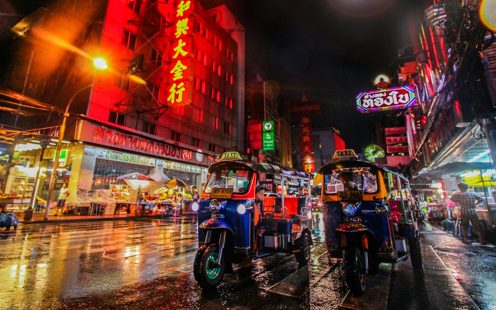 Two tuk-tuks parked on a neon-lit street in Bangkok's Chinatown at night
