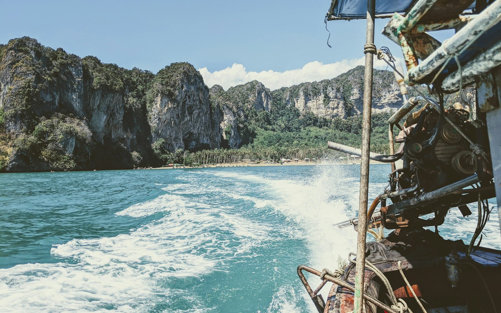 Wooden longtail boats moored below limestone cliffs on a calm turquoise bay in Southeast Asia