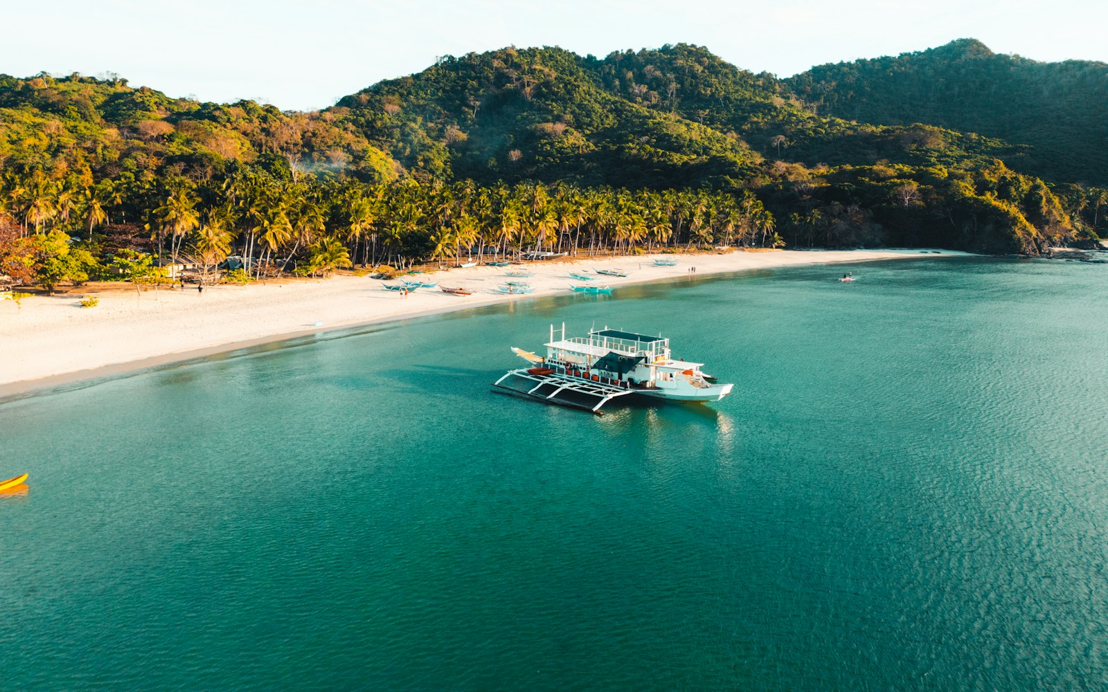 An outrigger boat on turquoise water beside a palm-covered island in the Philippines