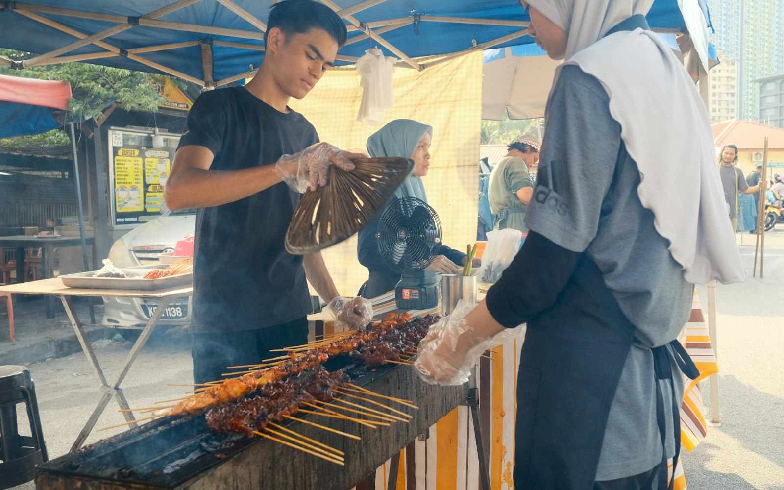 A vendor grilling satay skewers over charcoal at a street food stall in Penang, Malaysia
