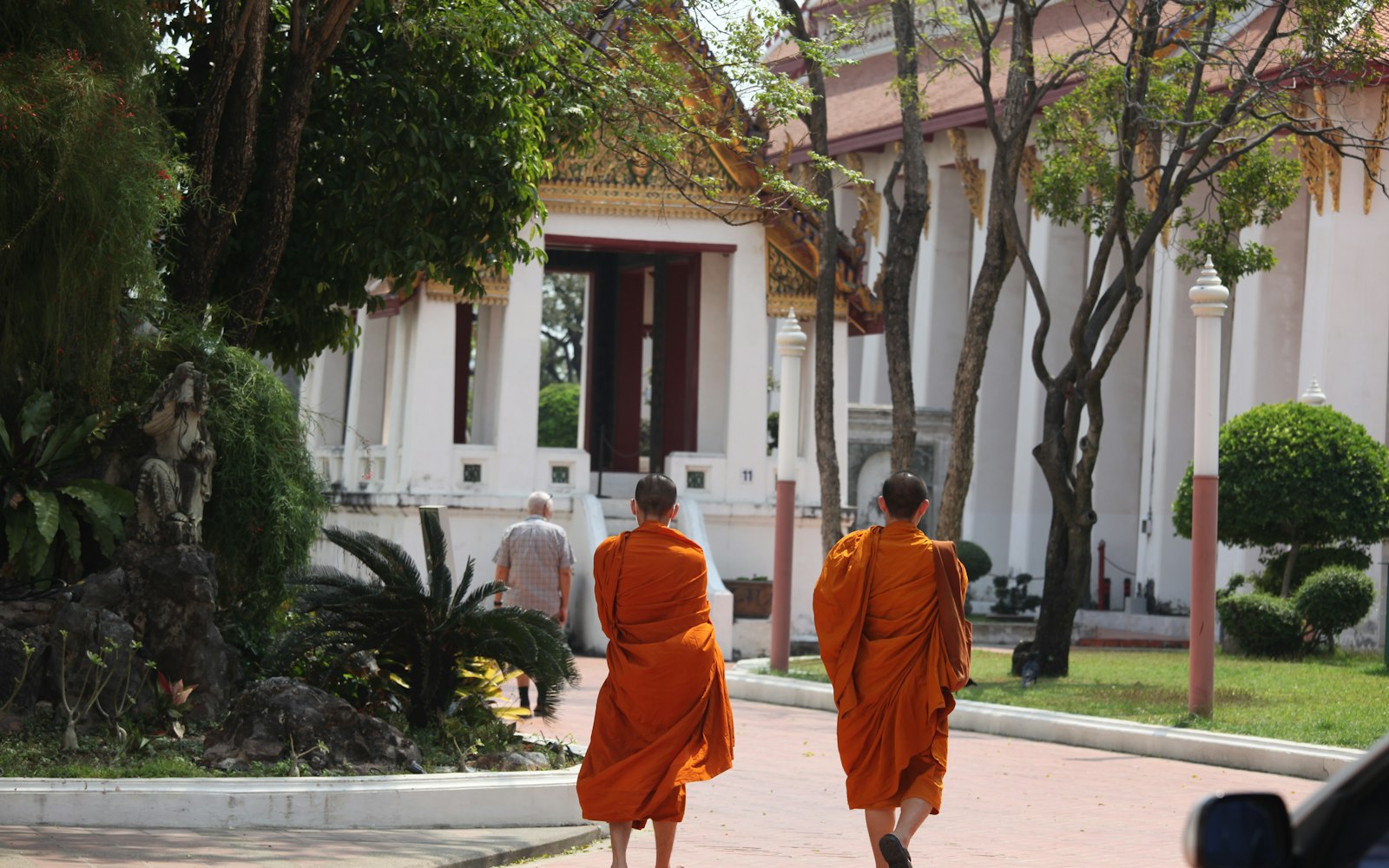 Two monks in orange robes walking toward a temple in Southeast Asia